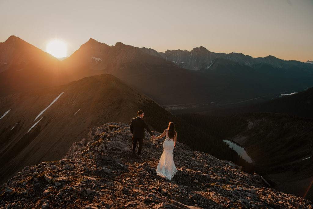 couple in wedding attire on top of a mountain at sunrise