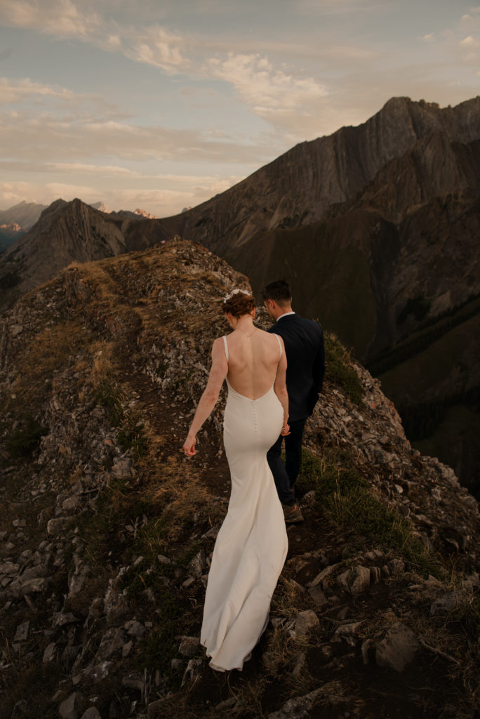 Wedding couple walking along a ridge on a mountain top at sunrise in Kananaskis